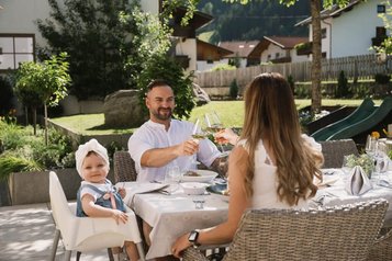 Familie genießt ein entspanntes Mittagessen auf der Terrasse des Familienhotels Alpenhotel Kindl bei Sonnenschein.