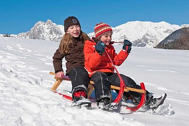 Kinder rodeln voller Freude die Piste hinunter in Südtirol im Familienhotel Alphotel Tyrol Wellness & Family Resort.
