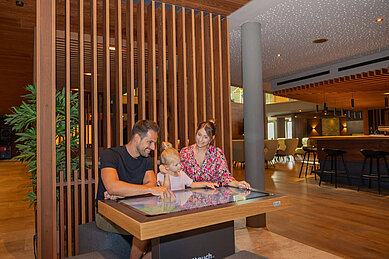 Familie spielt im Restaurant des Familienhotels Schreinerhof mit einem interaktiven Display.