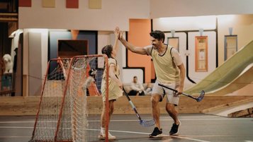 Ein Vater und eine Tochter spielen in einer Indoor-Sporthalle des Hotel Sonngastein im Salzburger Land gemeinsam Hockey.