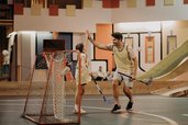 Ein Vater und eine Tochter spielen in einer Indoor-Sporthalle des Hotel Sonngastein im Salzburger Land gemeinsam Hockey.