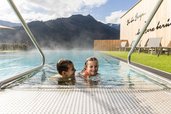Zwei Kinder planschen im beheizten Außenpool des Familienhotels Almfamilyhotel Scherer mit Blick auf die umliegenden Berge.