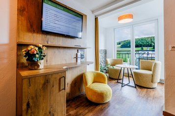 Moderner Wohnbereich mit Fernseher, Holzmöbeln, Sitzgruppe und Balkonblick im Hotel Engel im Schwarzwald