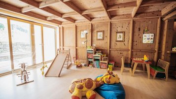 Heller Kinderspielraum mit Holzinterieur, Rutsche und Spielzeug im Wellness- & Familienhotel Egger.