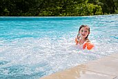 Kleines Mädchen mit Schwimmflügeln sitzt im Pool vom Familienhotel Engel Gourmet & Spa in Südtirol.