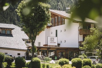 Sommerliche Außenansicht des Familienhotel Alpenhof Dolomit Family mit Garten und Teich.