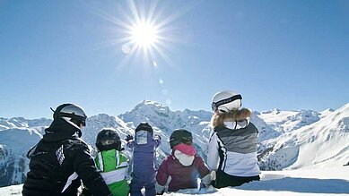 Familie sitzt in Skiausrüstung auf der Piste und ruht sich kurz aus, bevor es wieder ins Familienhotel Bella Vista in Südtirol geht.