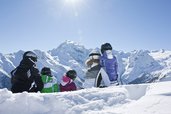 Familie sitzt in Skiausrüstung auf der Piste und ruht sich kurz aus, bevor es wieder ins Familienhotel Bella Vista in Südtirol geht.