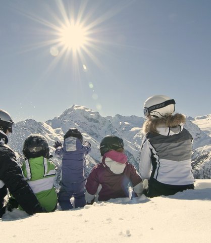Familie sitzt in Skiausrüstung auf der Piste und ruht sich kurz aus, bevor es wieder ins Familienhotel Bella Vista in Südtirol geht.