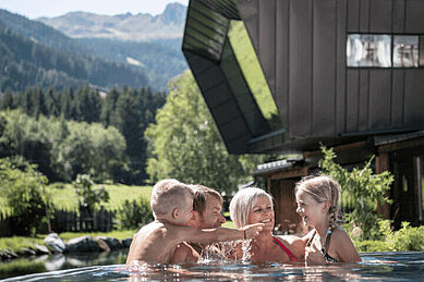 Familie planscht im Außenpool der Mons Silva Private Luxury Chalets im Familienurlaub in Südtirol.