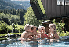 Familie planscht im Außenpool der Mons Silva Private Luxury Chalets im Familienurlaub in Südtirol.