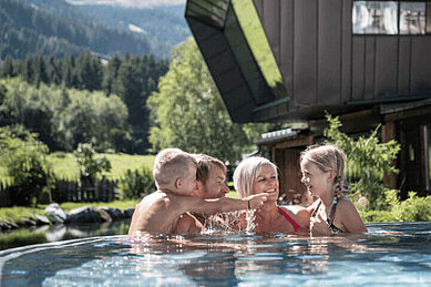 Familie planscht im Außenpool der Mons Silva Private Luxury Chalets im Familienurlaub in Südtirol.