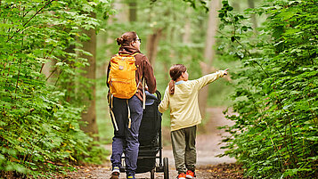 Wandern im Thüringer Wald: Mutter mit Kind und Kinderwagen laufen durch eine Waldpromenade.