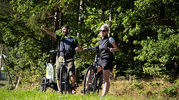 Zwei Eltern mit Kinder-Fahrradanhänger bei einer Fahrradtour im Familienurlaub im Böhmerwald.