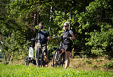 Zwei Eltern mit Kinder-Fahrradanhänger bei einer Fahrradtour im Familienurlaub im Böhmerwald.