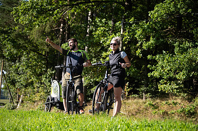 Zwei Eltern mit Kinder-Fahrradanhänger bei einer Fahrradtour im Familienurlaub im Böhmerwald.