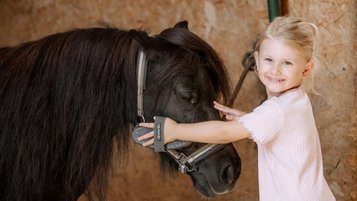 Mädchen streichelt ein Pony im Reitstall des Familienhotels Schreinerhof im Bayerischen Wald.