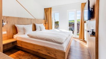 Helles Schlafzimmer mit Doppelbett aus Holz, Balkonzugang und Blick ins Grüne im Hotel Engel im Schwarzwald