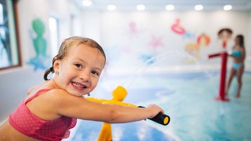 Mädchen spielt auf dem Wasserspielplatz im Hallenbad des Familienhotels Kirchheimerhof in Kärnten mit einer Wasserpistole.