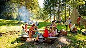 Familien lassen den Tag bei Lagerfeuer und Stockbrot auf dem Waldspielplatz des Familienhotel Spa- & Familien-Resorts Krone im Allgäu ausklingen.