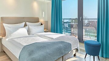 Doppelbett mit Zimmer mit Aussicht nach draußen mit viel Tageslicht im Familienhotel Strandkind an der Ostsee