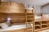 Gemütliches Familienzimmer im Hotel Zauchenseehof mit maßgefertigten Stockbetten aus hellem Holz, integrierten Ablagefächern und einer verspielten Waldtapete mit kleinen Eulenmotiven im Hintergrund.