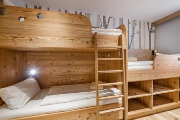 Gemütliches Familienzimmer im Hotel Zauchenseehof mit maßgefertigten Stockbetten aus hellem Holz, integrierten Ablagefächern und einer verspielten Waldtapete mit kleinen Eulenmotiven im Hintergrund.