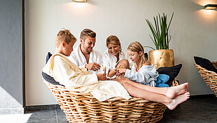 Familie sitzt im gemeinsam im Wellnessbereich des Familienhotels Amiamo in Zell am See. Alle tragen einen Bademantel und genießen die gemeinsame Familienzeit.