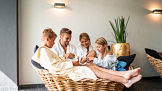 Familie sitzt im gemeinsam im Wellnessbereich des Familienhotels Amiamo in Zell am See. Alle tragen einen Bademantel und genießen die gemeinsame Familienzeit.