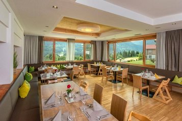 Heller Speisesaal mit großen Fenstern und Kindersitzmöglichkeiten im Familienhotel mit Blick auf die Berge