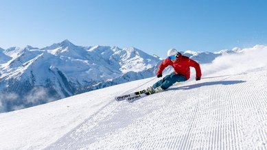 Skifahrer auf einer Piste nahe dem Hotel Sonngastein im Salzburger Land mit verschneitem Bergpanorama.
