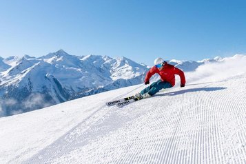 Skifahrer auf einer Piste nahe dem Hotel Sonngastein im Salzburger Land mit verschneitem Bergpanorama.