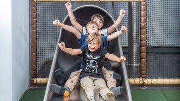 Drei Kinder rutschen lachend gemeinsam eine rutsche im Familienhotel hinunter.