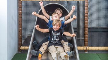 Drei Kinder rutschen lachend gemeinsam eine rutsche im Familienhotel hinunter.