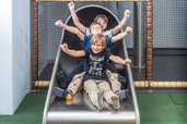 Drei Kinder rutschen lachend gemeinsam eine rutsche im Familienhotel hinunter.