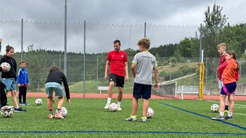 Kinder und Jugendtrainer beim Fußballtraining auf einem Kunstrasenplatz im Freien.