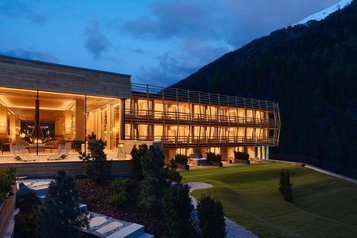 Beleuchteter Neubau des Familienhotel Bella Vista in Südtirol bei Nacht mit Terrasse, Garten und Bergkulisse.