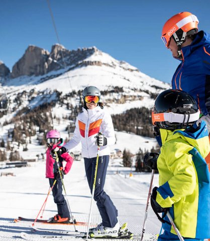 Familie steht fröhlich auf er Piste und genießt die Aussicht auf die Dolomiten.