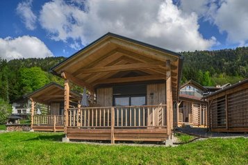 Ein gemütliches Tiny House aus Holz mit Veranda steht im Grünen beim Familienhotel Ramsi inmitten der Kärntner Berglandschaft