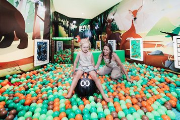 Ein Kind und eine Frau spielen gemeinsam im bunt beleuchteten Bällebad mit Waldtiermotiven im Familienhotel Tirolerhof.