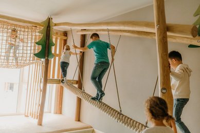 Im Spielbereich des Familienhotel Friedrichshof balancieren Kinder auf einer Hängebrücke aus Seilen.