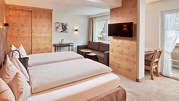 Gemütliches Zimmer im Hotel Habachklause mit natürlicher Holzvertäfelung, einem weichen Doppelbett und einer Sitzecke, nahe einem Fenster mit Blick auf die verschneite Landschaft.