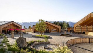 Der ErlebnisHof des Familienhotels Allgäuer Berghof im Allgäu zeigt mehrere Holzgebäude, Spielbereiche und einen zentralen Platz vor der Bergkulisse.