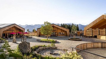 Der ErlebnisHof des Familienhotels Allgäuer Berghof im Allgäu zeigt mehrere Holzgebäude, Spielbereiche und einen zentralen Platz vor der Bergkulisse.
