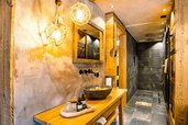 Modernes Badezimmer mit Naturmaterialien, Holzwaschtisch, Steinwaschbecken, beleuchtetem Spiegel und begehbarer Regendusche im Alpura Retreat.