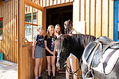 Mädchen stehen vor der Reithalle des Familienhotels Böhmerwald und streicheln ein Pferd.