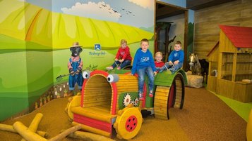 Bunter Indoor-Spielplatz im Farmland-Stil mit großem Kindertraktor, Spielhaus und weichem Boden – ideal für kreatives Spielen und Bewegung.