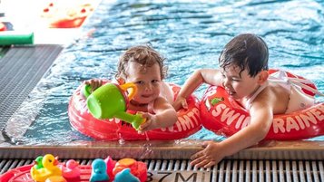 Zwei Kleinkinder planschen fröhlich mit Schwimmringen und Wasserspielzeug im Poolbereich des Familienhotels Ramsi in Kärnten