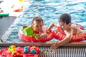 Zwei Kleinkinder planschen fröhlich mit Schwimmringen und Wasserspielzeug im Poolbereich des Familienhotels Ramsi in Kärnten