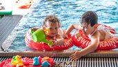 Zwei Kleinkinder planschen fröhlich mit Schwimmringen und Wasserspielzeug im Poolbereich des Familienhotels Ramsi in Kärnten